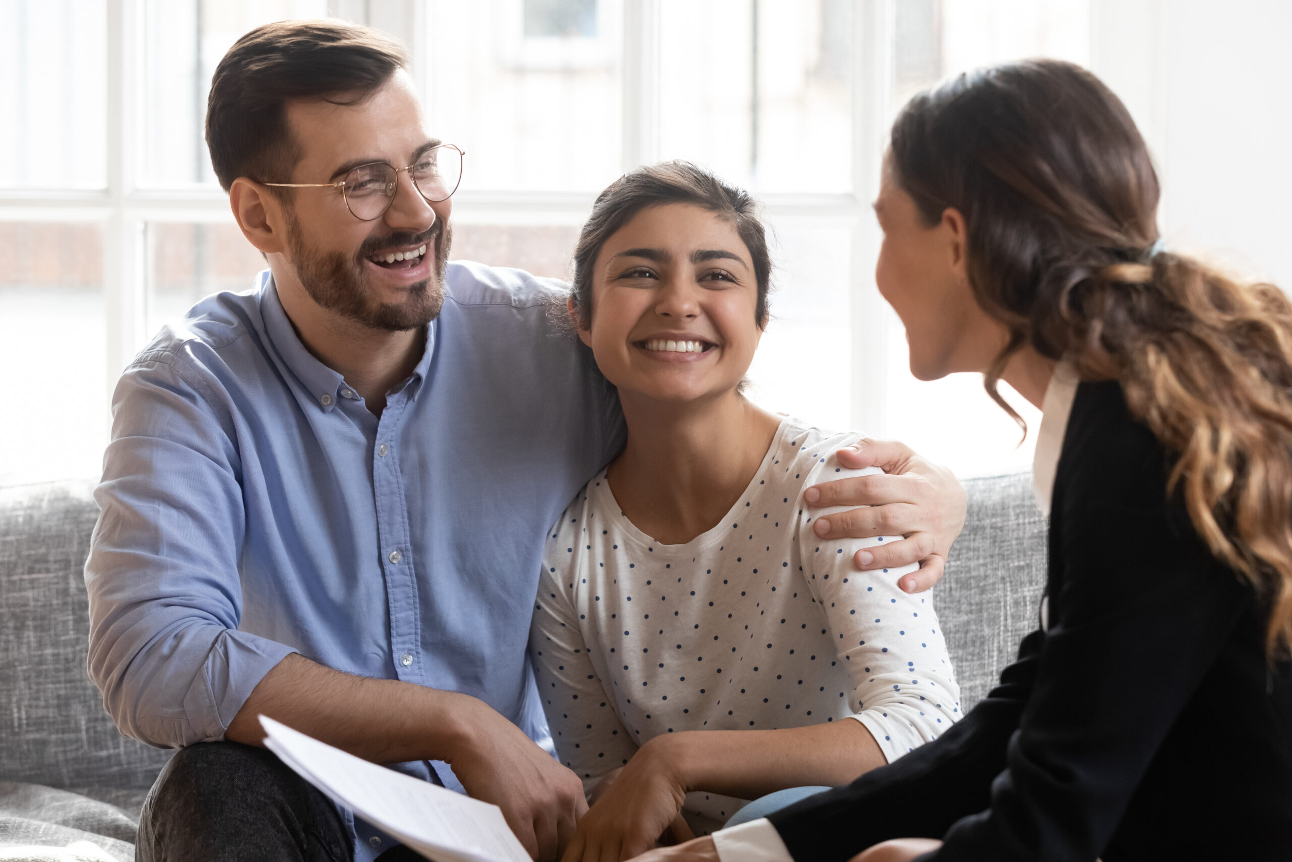 A man and woman smile at a woman sitting between them, fostering a warm and engaging conversation in a cozy setting.